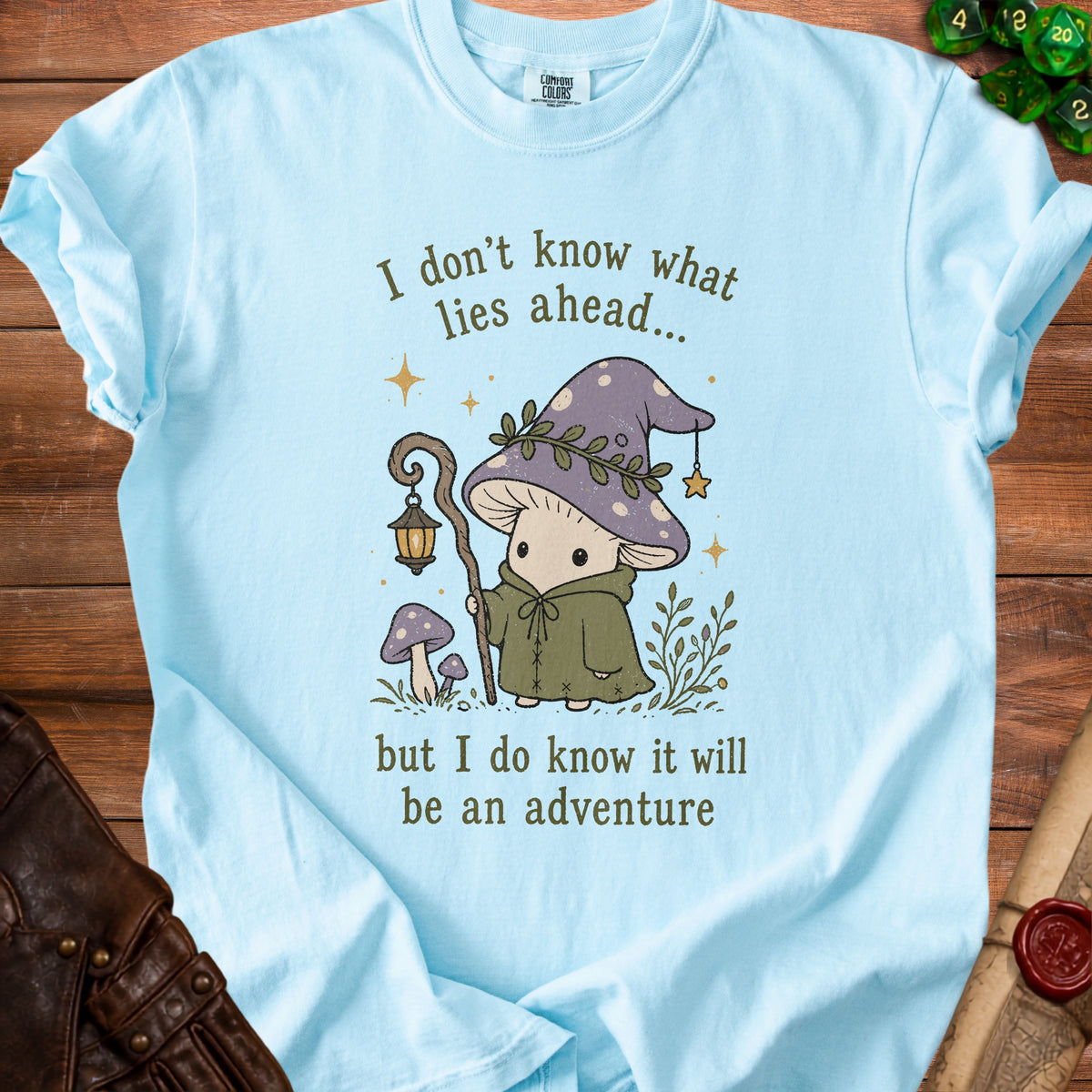 Light blue t-shirt with a wizard mushroom graphic and text "I don't know what lies ahead... but I do know it will be an adventure".