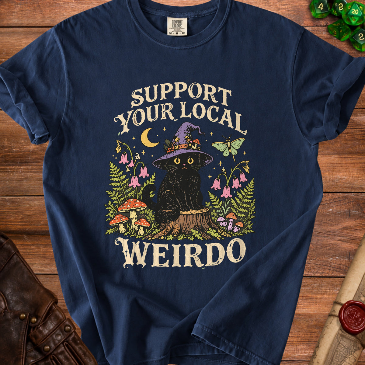 Navy blue t-shirt featuring a witch cat on a tree stump with mushrooms and the text "SUPPORT YOUR LOCAL WEIRDO."