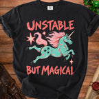Black t-shirt with teal unicorn, pink mane, and text "UNSTABLE BUT MAGICAL".