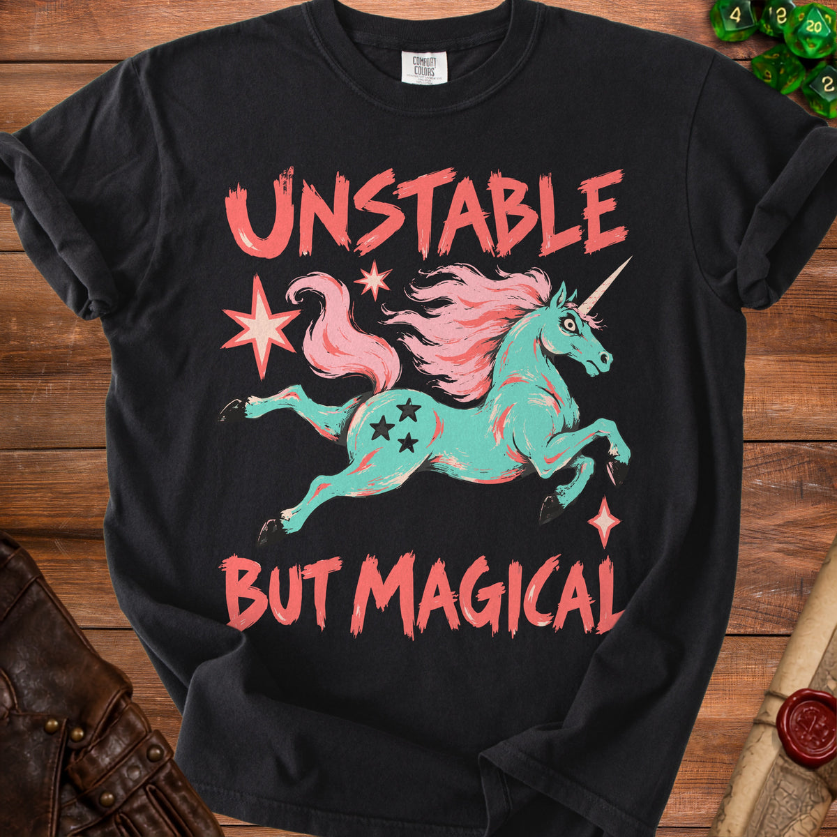 Black t-shirt with teal unicorn, pink mane, and text "UNSTABLE BUT MAGICAL".