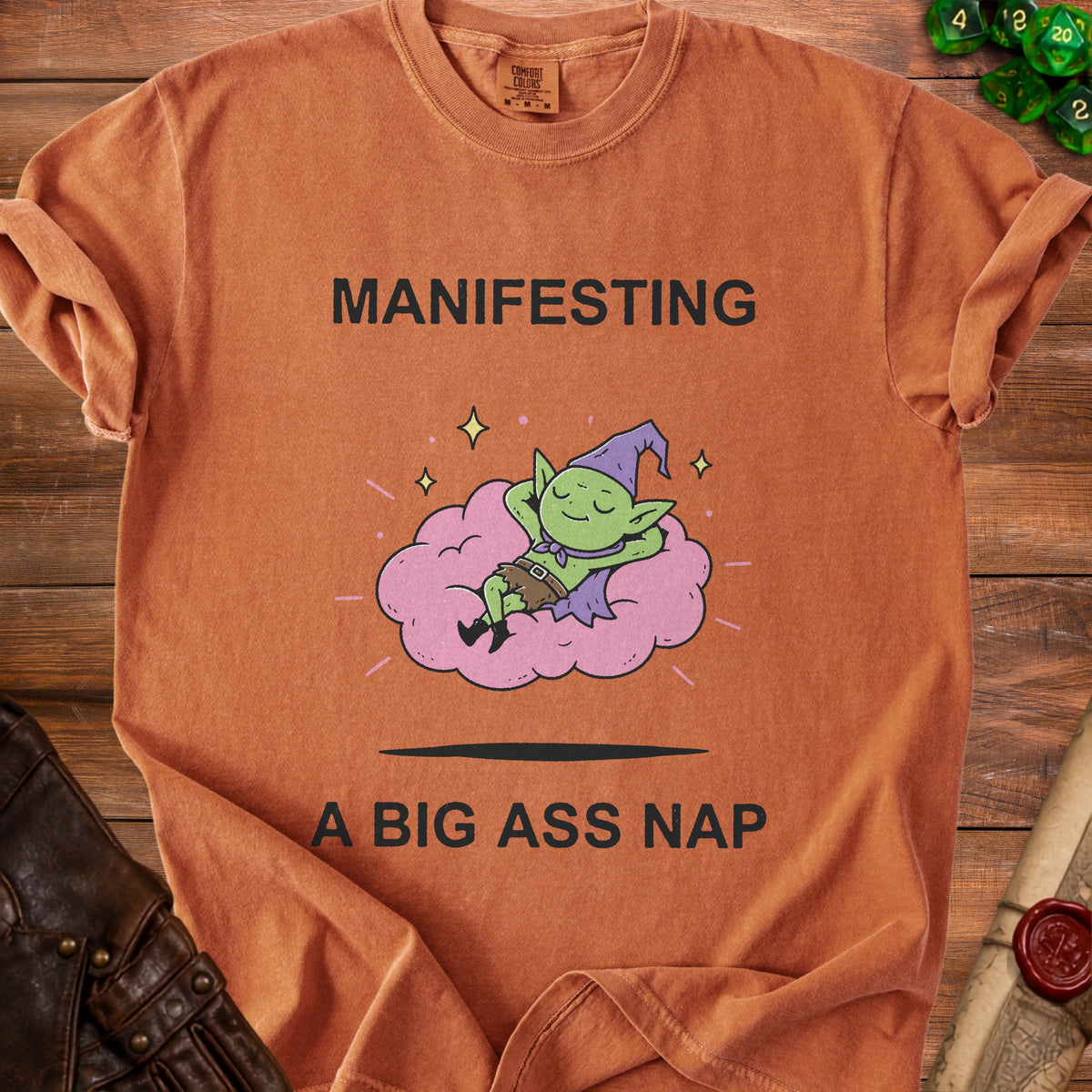 Orange t-shirt with text "MANIFESTING A BIG ASS NAP" and a sleeping green goblin.