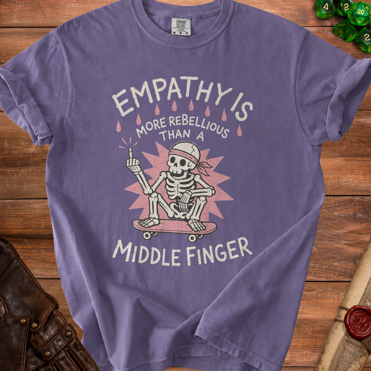 Purple t-shirt with skeleton on skateboard giving middle finger, text reads "EMPATHY IS MORE REBELLIOUS THAN A MIDDLE FINGER".