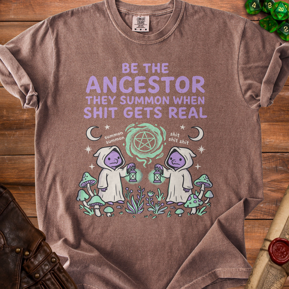 Brown t-shirt with "BE THE ANCESTOR THEY SUMMON WHEN SHIT GETS REAL" text and cartoon characters.
