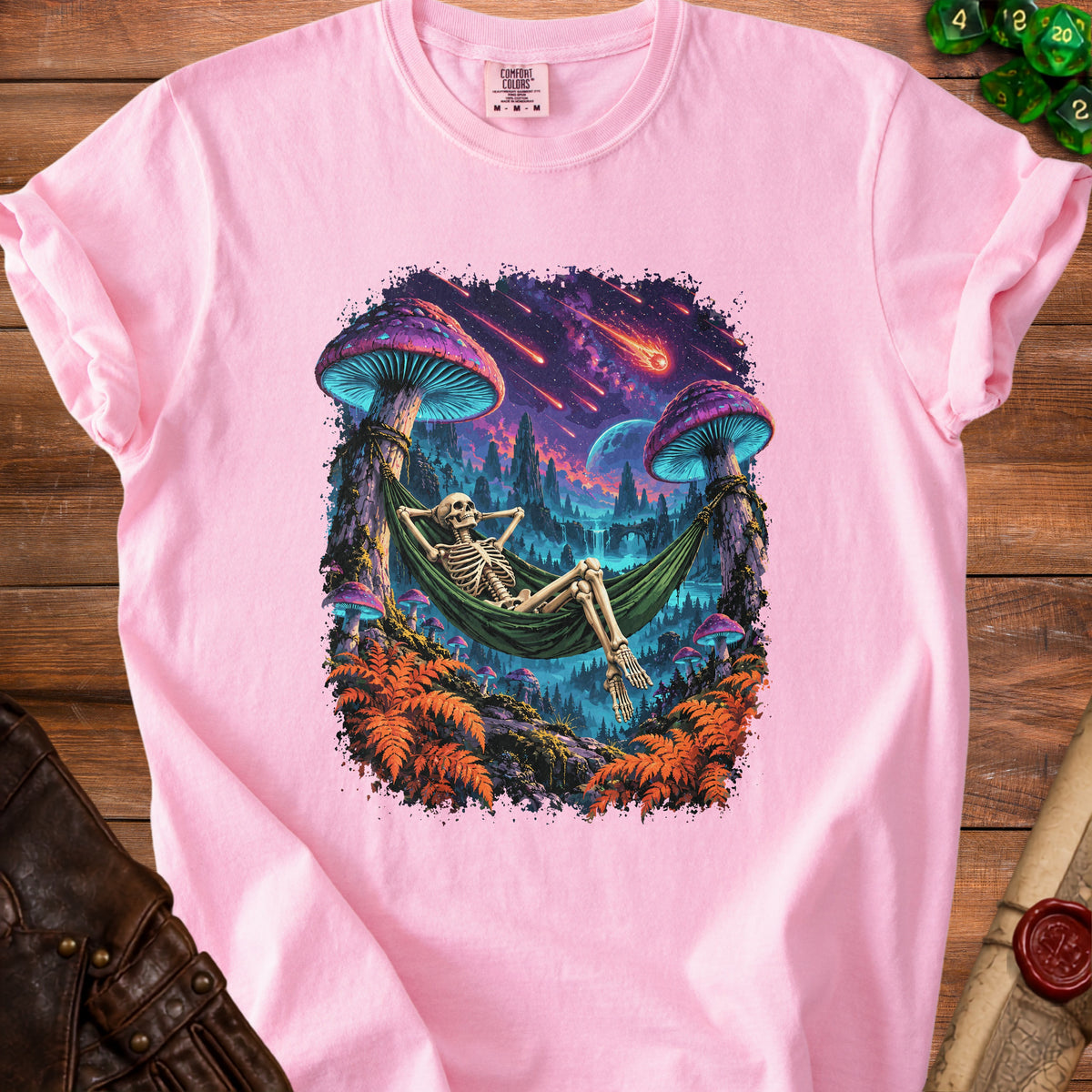 Pink t-shirt with graphic of skeleton in hammock under mushrooms with meteor shower.