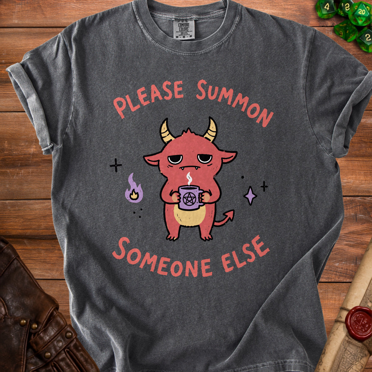 Dark gray t-shirt with a cartoon demon holding a pentagram mug, text says "Please summon someone else".