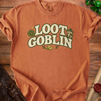 Orange t-shirt with "LOOT GOBLIN" text, mushrooms, dice, and coins.