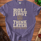 Purple t-shirt with "Roll First Think Later" and a d20 die.