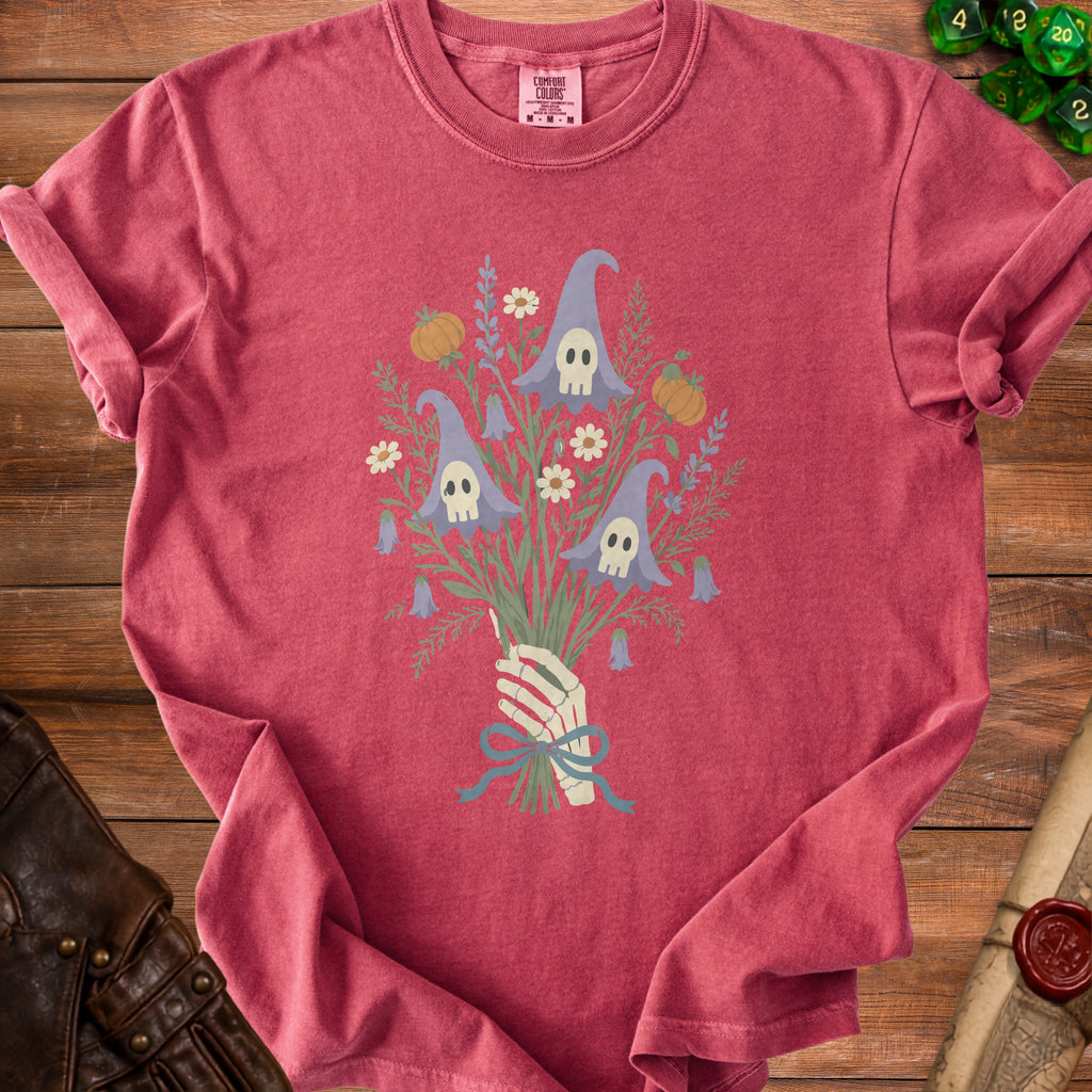 Pink t-shirt with skeleton hand holding bouquet of gnome-shaped skulls, pumpkins, and flowers.