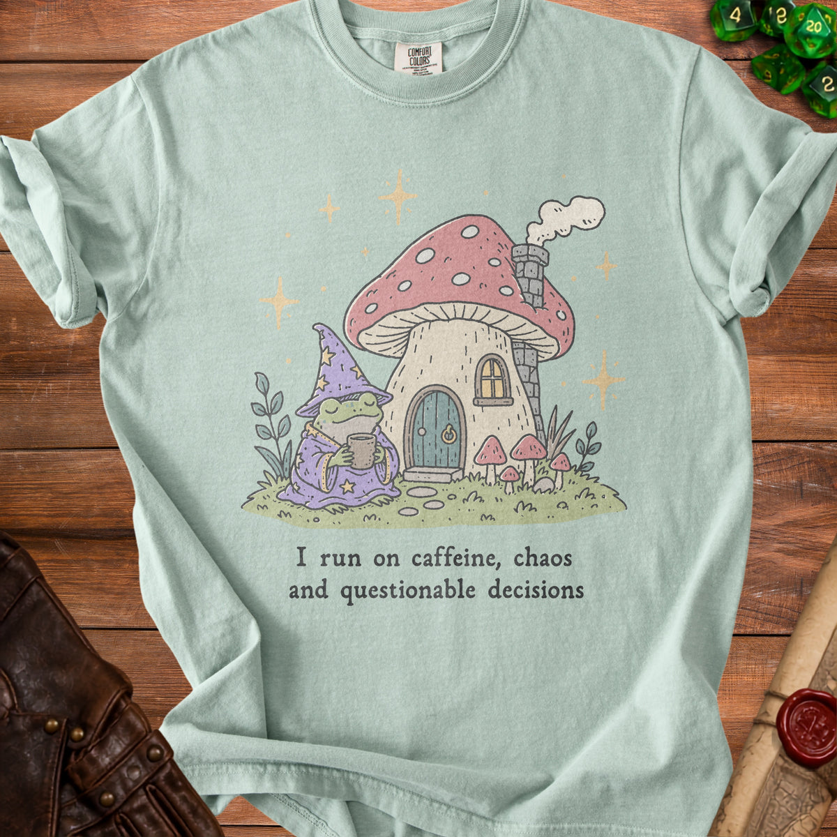 Light blue t-shirt with frog wizard and mushroom house graphic and text "I run on caffeine, chaos and questionable decisions."