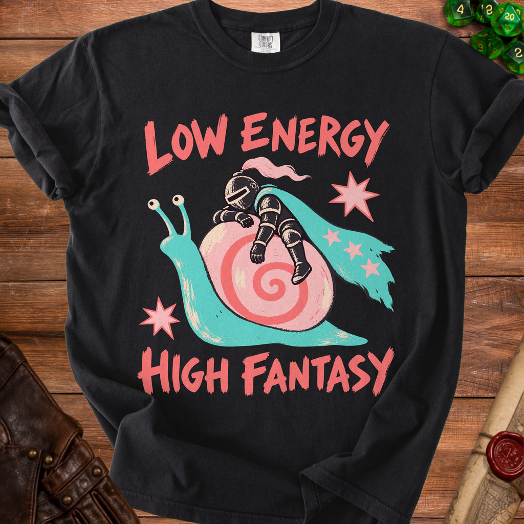 A black t-shirt features a graphic of a knight sleeping on a snail's shell, with text reading LOW ENERGY HIGH FANTASY.