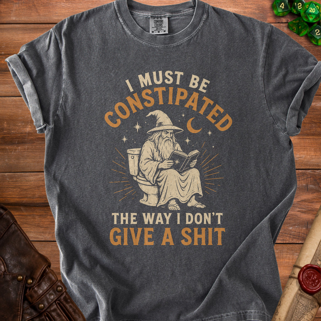 Dark gray t-shirt with a wizard on a toilet reading and the text "I MUST BE CONSTIPATED THE WAY I DON'T GIVE A SHIT".