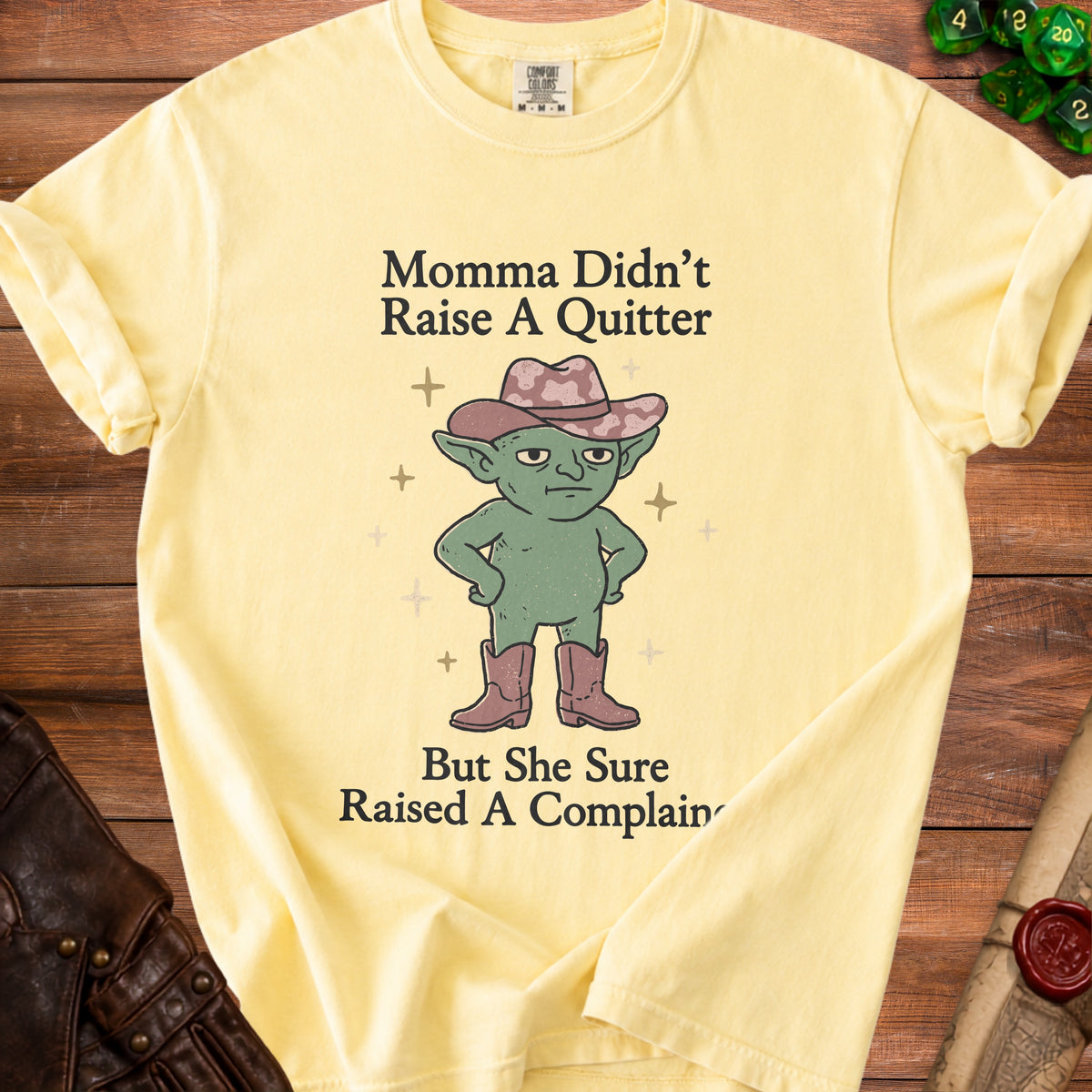 Yellow t-shirt with green goblin wearing cowboy hat and boots, saying "Momma Didn't Raise A Quitter But She Sure Raised A Complain".