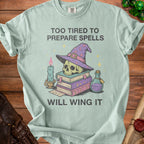 Light blue t-shirt with skull, witch hat, candle, books, and potion. Text reads: Too tired to prepare spells will wing it.