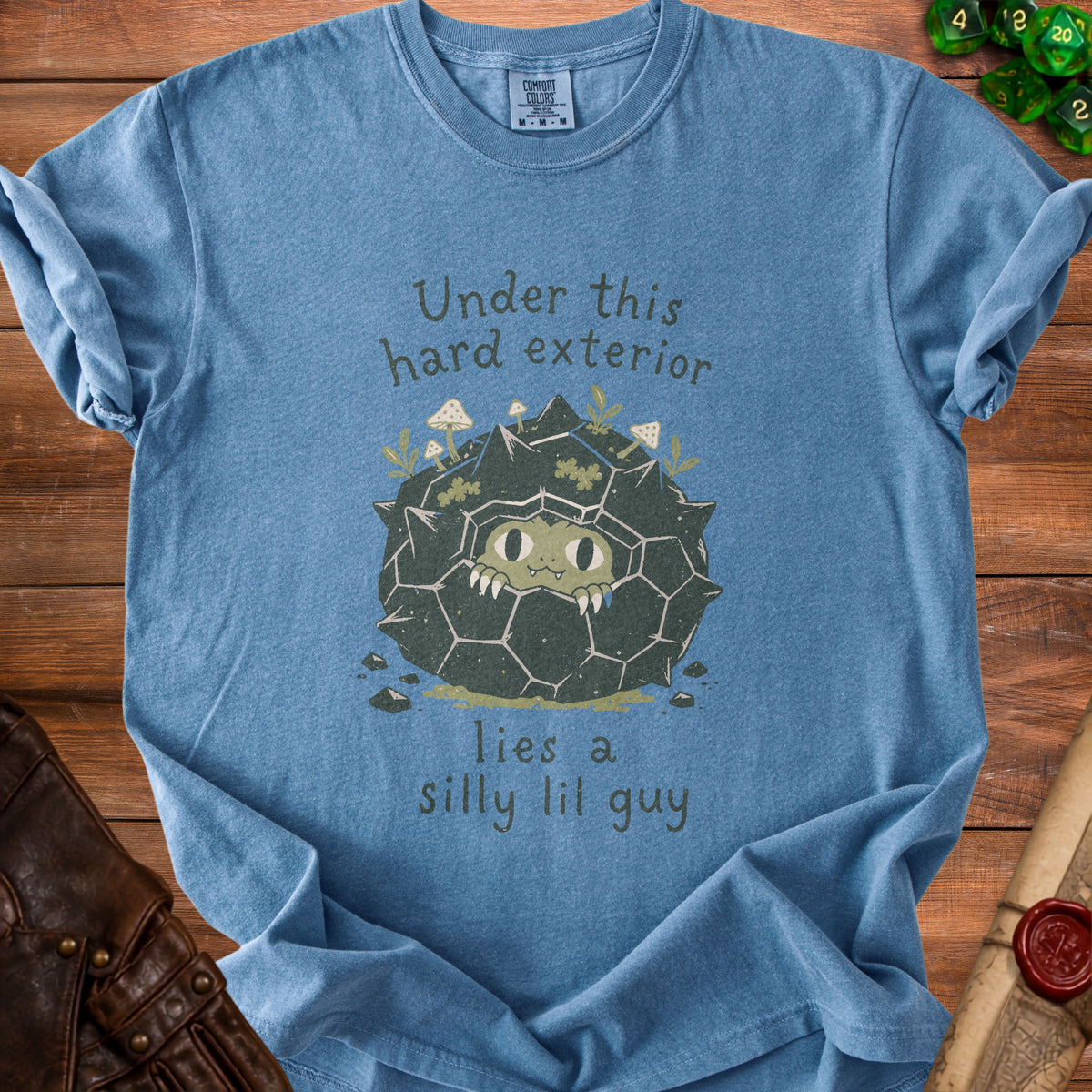 Blue t-shirt with a graphic of a spiky creature saying "Under this hard exterior lies a silly lil guy."