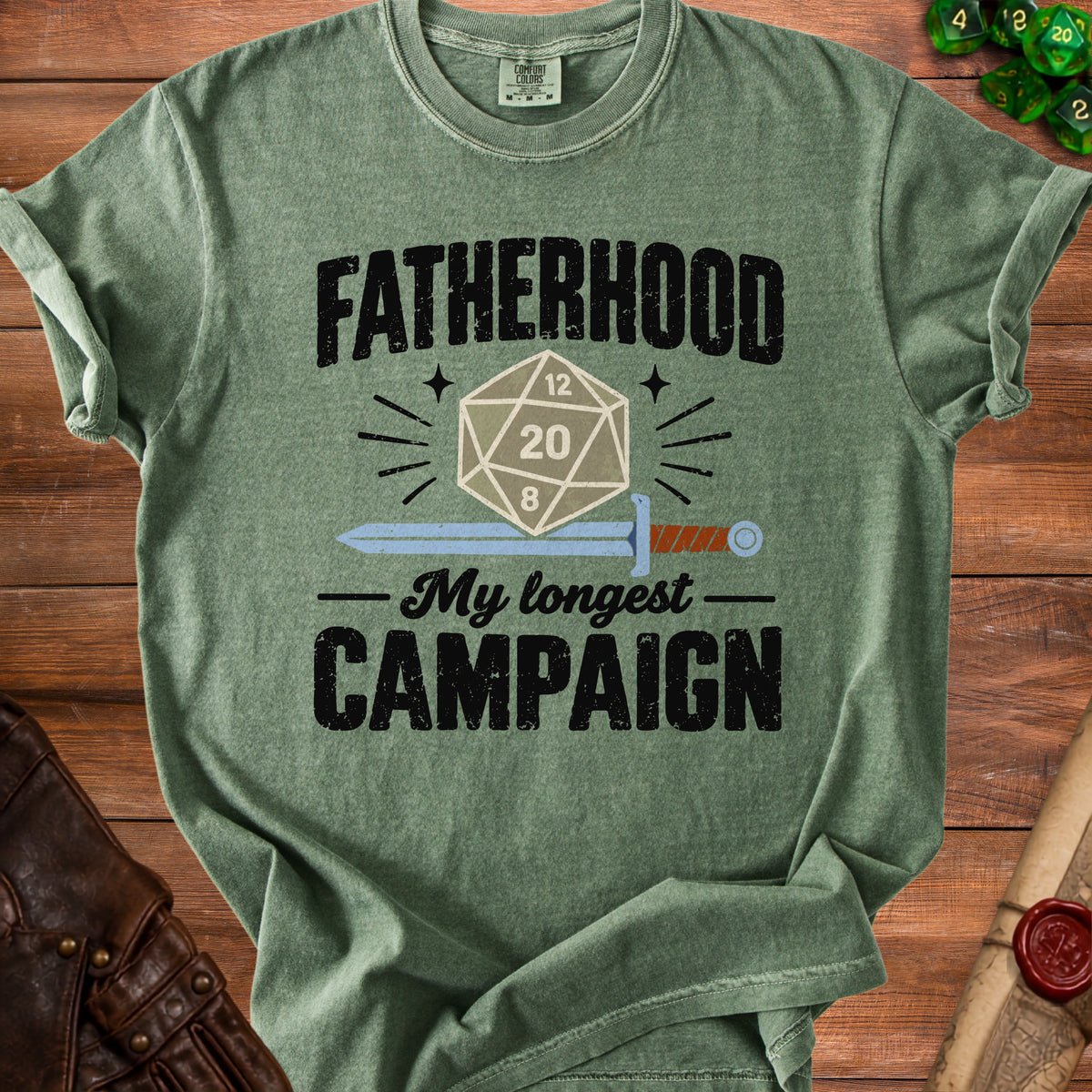 Green t-shirt with "FATHERHOOD" and "My longest CAMPAIGN" text, D20 die, and sword graphic.