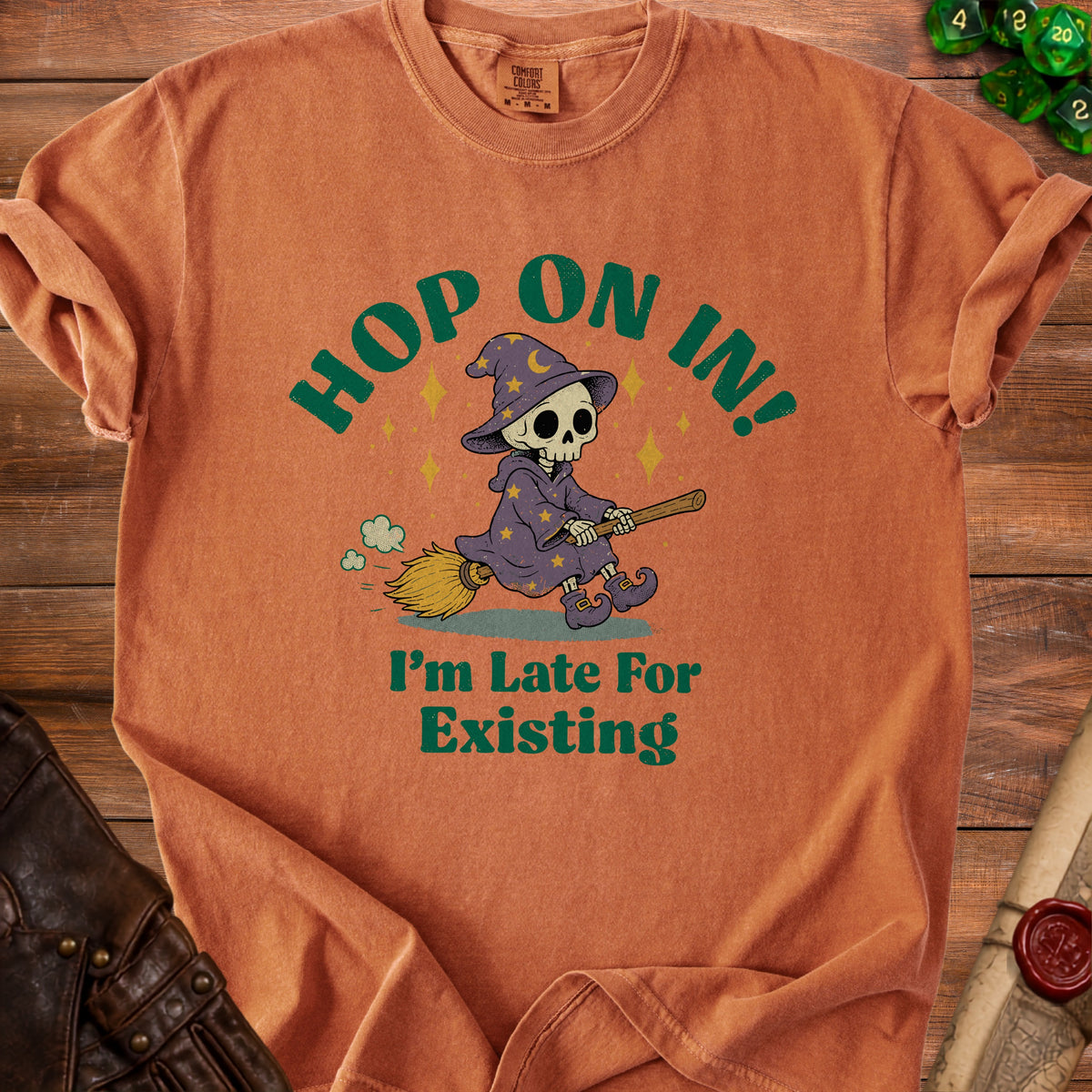 Orange t-shirt with graphic of skeleton wizard on broom and text "Hop on in! I'm late for existing."