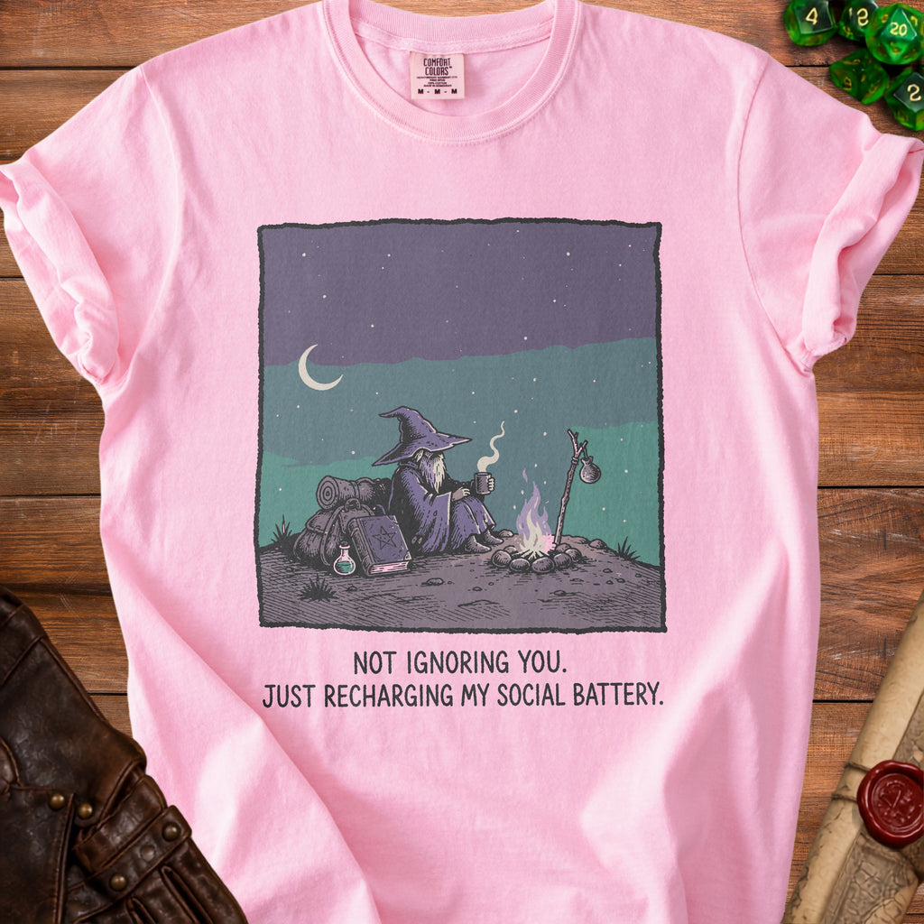 Pink t-shirt with graphic of wizard by campfire, text "NOT IGNORING YOU. JUST RECHARGING MY SOCIAL BATTERY."