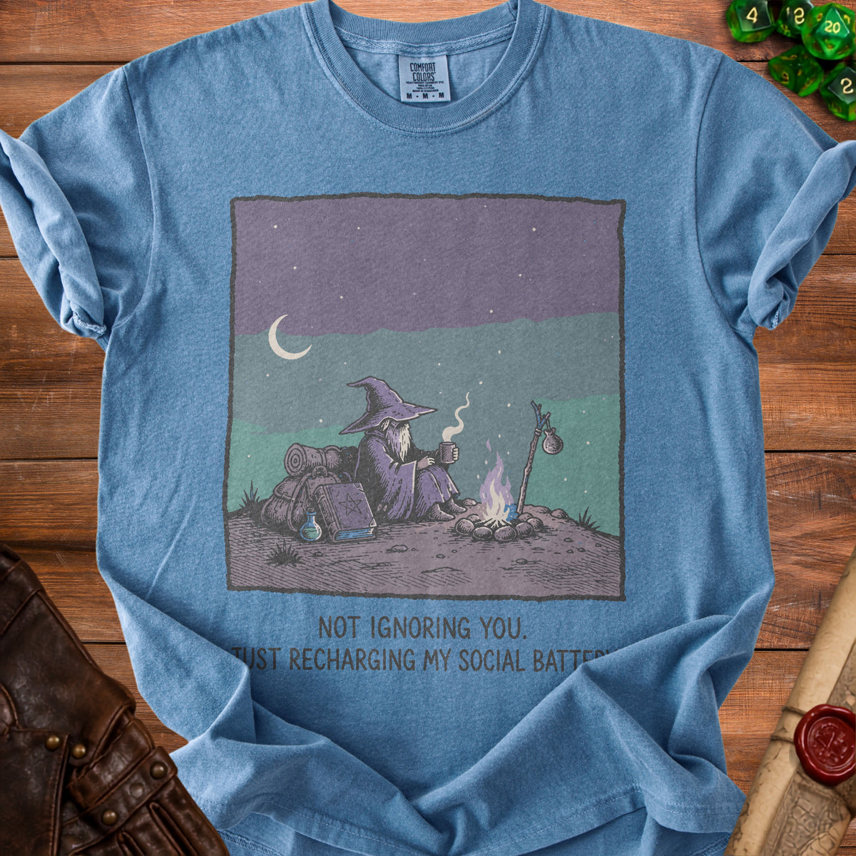 Blue t-shirt with wizard by campfire graphic and text "NOT IGNORING YOU. JUST RECHARGING MY SOCIAL BATTERY."