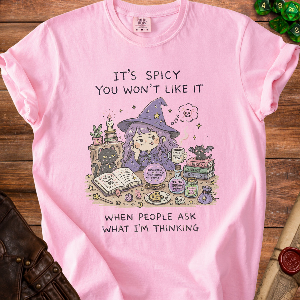 Pink t-shirt with illustration of a witch, black cat, spell books, and text "It's spicy you won't like it when people ask what I'm thinking".