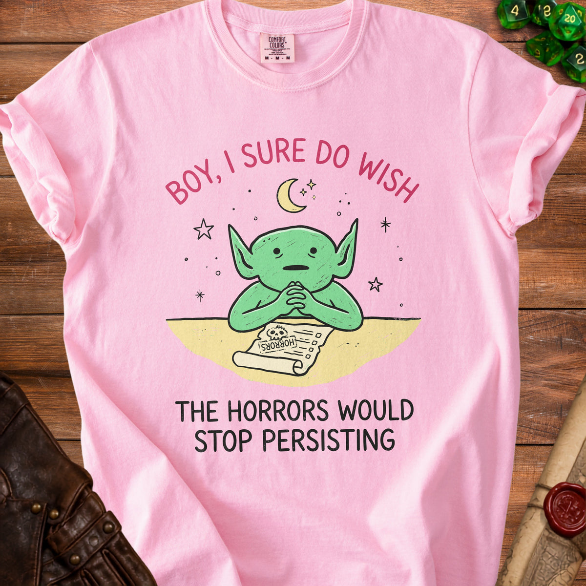 Pink t-shirt with a green cartoon creature and the text "Boy, I sure do wish the horrors would stop persisting."