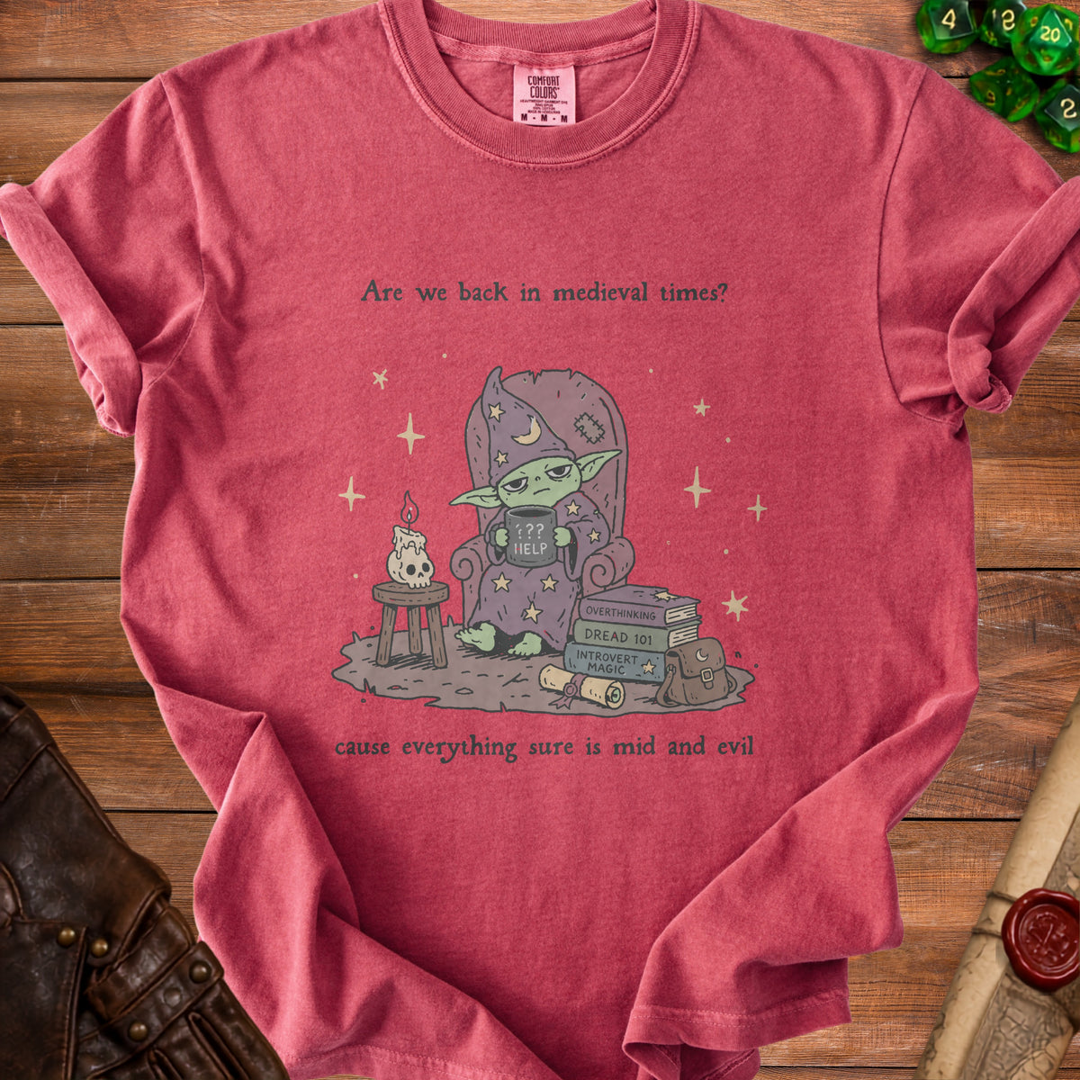 T-shirt graphic with a wizard character, books, and text "Are we back in medieval times? cause everything sure is mid and evil".