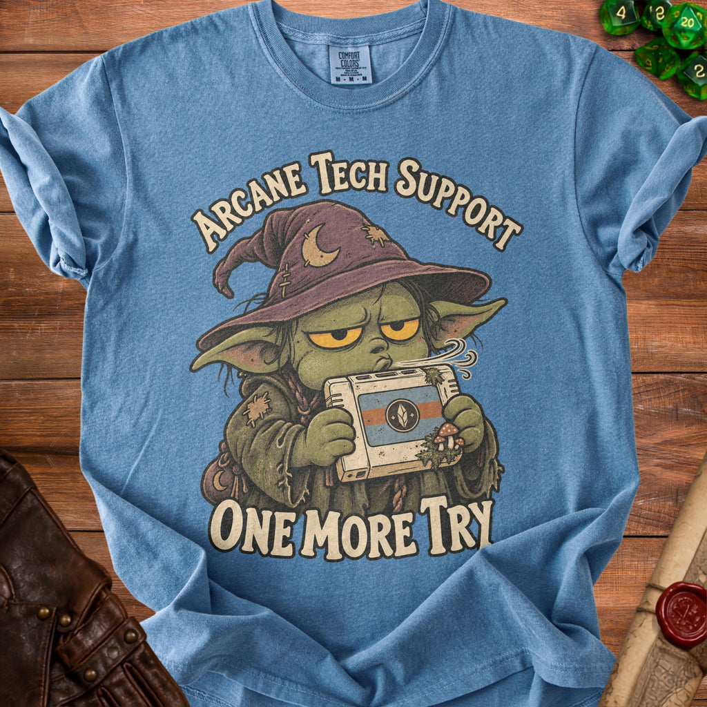 Blue t-shirt with a wizard character holding a video game console, reads "Arcane Tech Support One More Try".