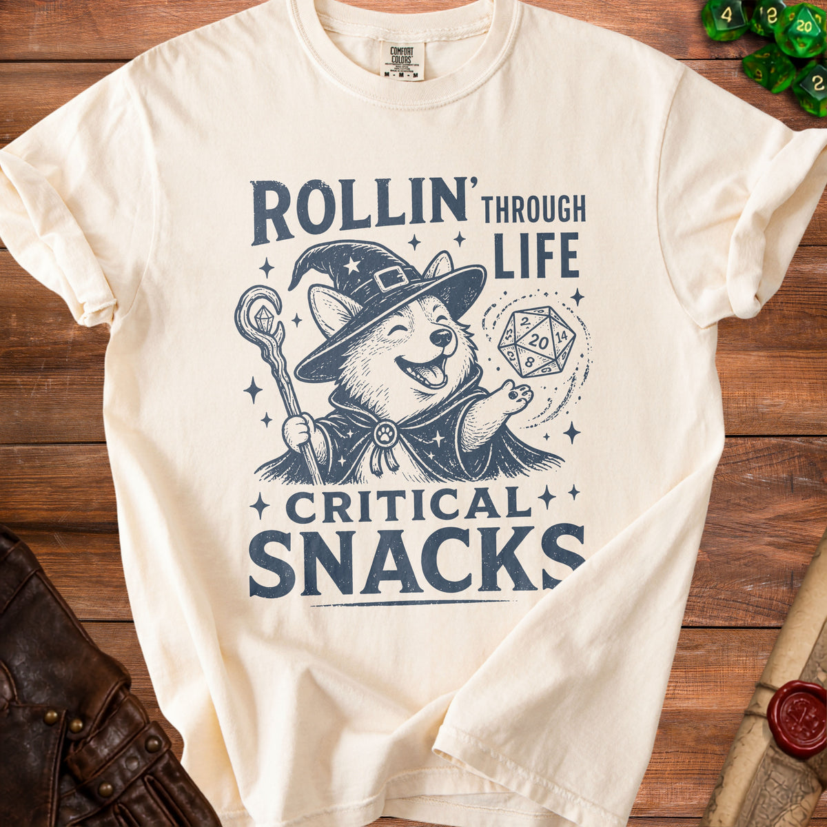 Cream t-shirt with a corgi wizard holding a staff and a d20 dice, text reads "Rollin' Through Life Critical Snacks".