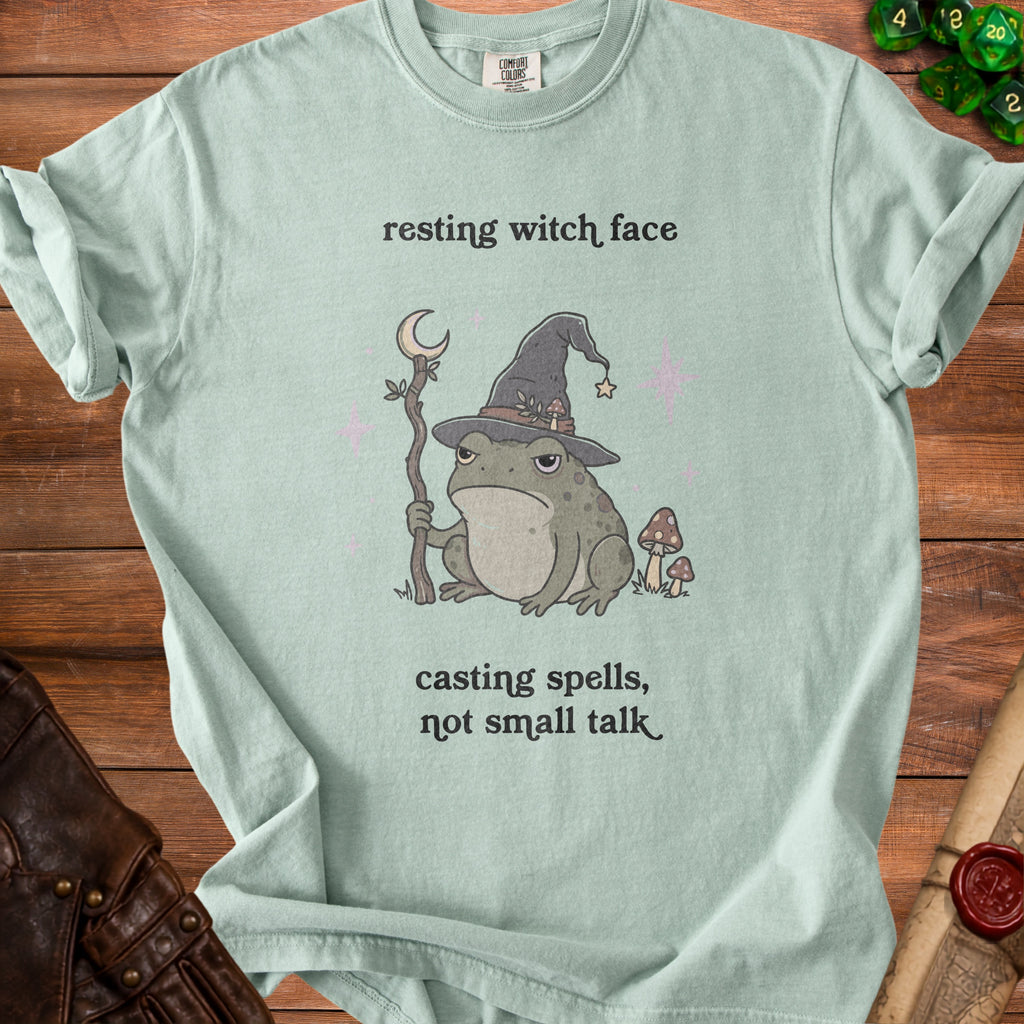 Light green t-shirt with a grumpy wizard frog and text "resting witch face, casting spells, not small talk."