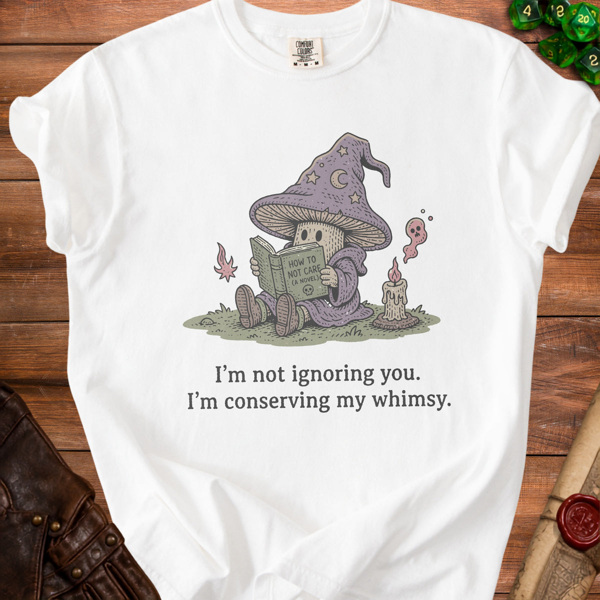 White t-shirt with graphic of a mushroom wizard reading "How to Not Care" with text "I'm not ignoring you. I'm conserving my whimsy."