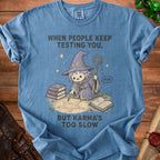 Blue t-shirt with a cartoon wizard casting a spell, text reads "When people keep testing you, but karma's too slow."