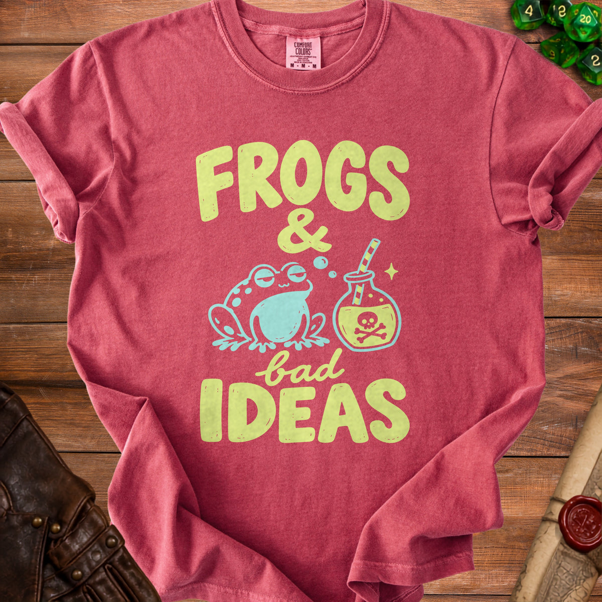 A red crewneck t-shirt with lime green text reading "FROGS & bad IDEAS," featuring a graphic of a frog and a poison bottle.