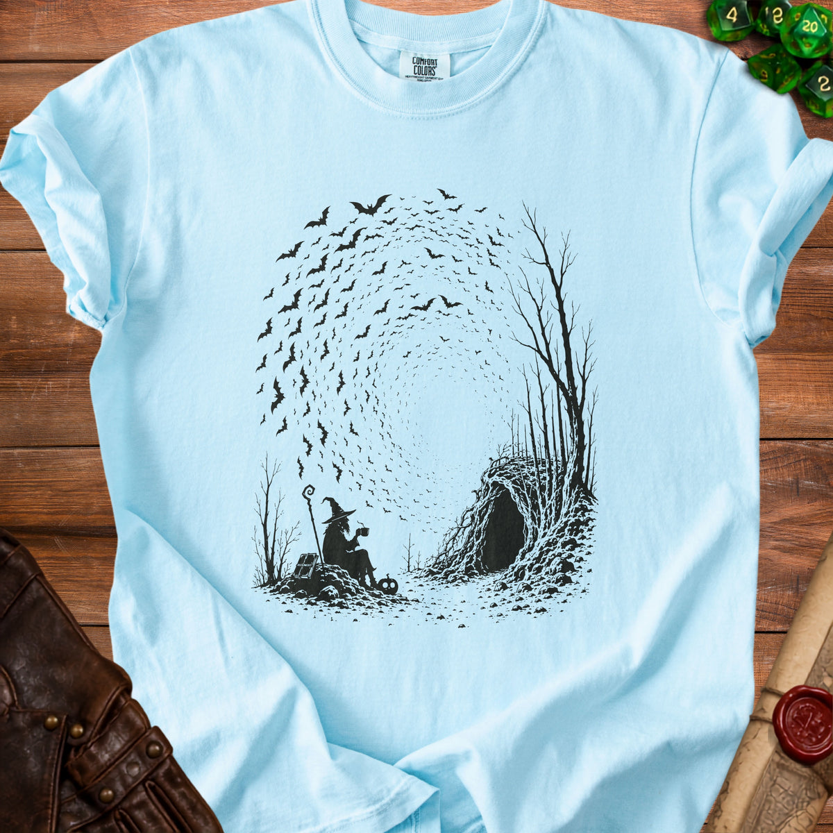 Silhouette of a witch with a hat and coffee mug in front of a cave entrance with swirling bats.