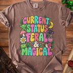 Brown t-shirt with "Current Status Feral & Magical" graphic and fantasy elements.