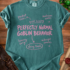 Teal t-shirt with pink text "PERFECTLY NORMAL GOBLIN BEHAVIOR" and related phrases.