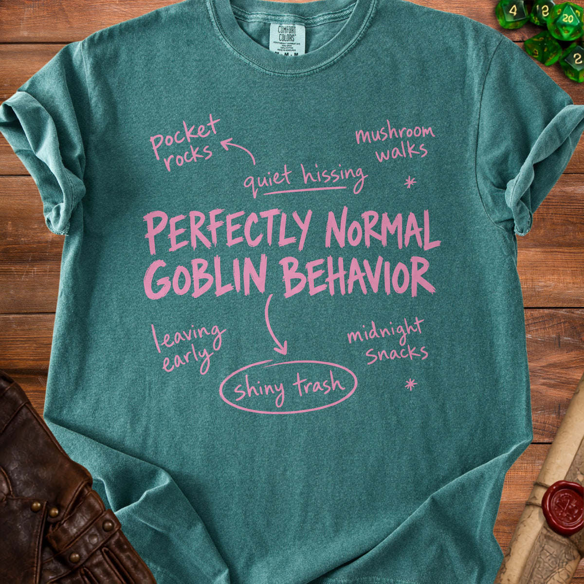 Teal t-shirt with pink text "PERFECTLY NORMAL GOBLIN BEHAVIOR" and related phrases.
