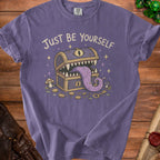 Purple t-shirt with "Just Be Yourself" text and a monster treasure chest graphic.