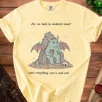 Yellow t-shirt with cartoon dragon on throne, text "Are we back in medieval times? cause everything sure is mid and".