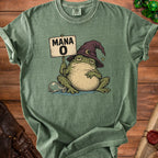 An olive green t-shirt featuring a graphic of a sleepy frog wearing a wizard hat and holding a sign that says MANA 0.
