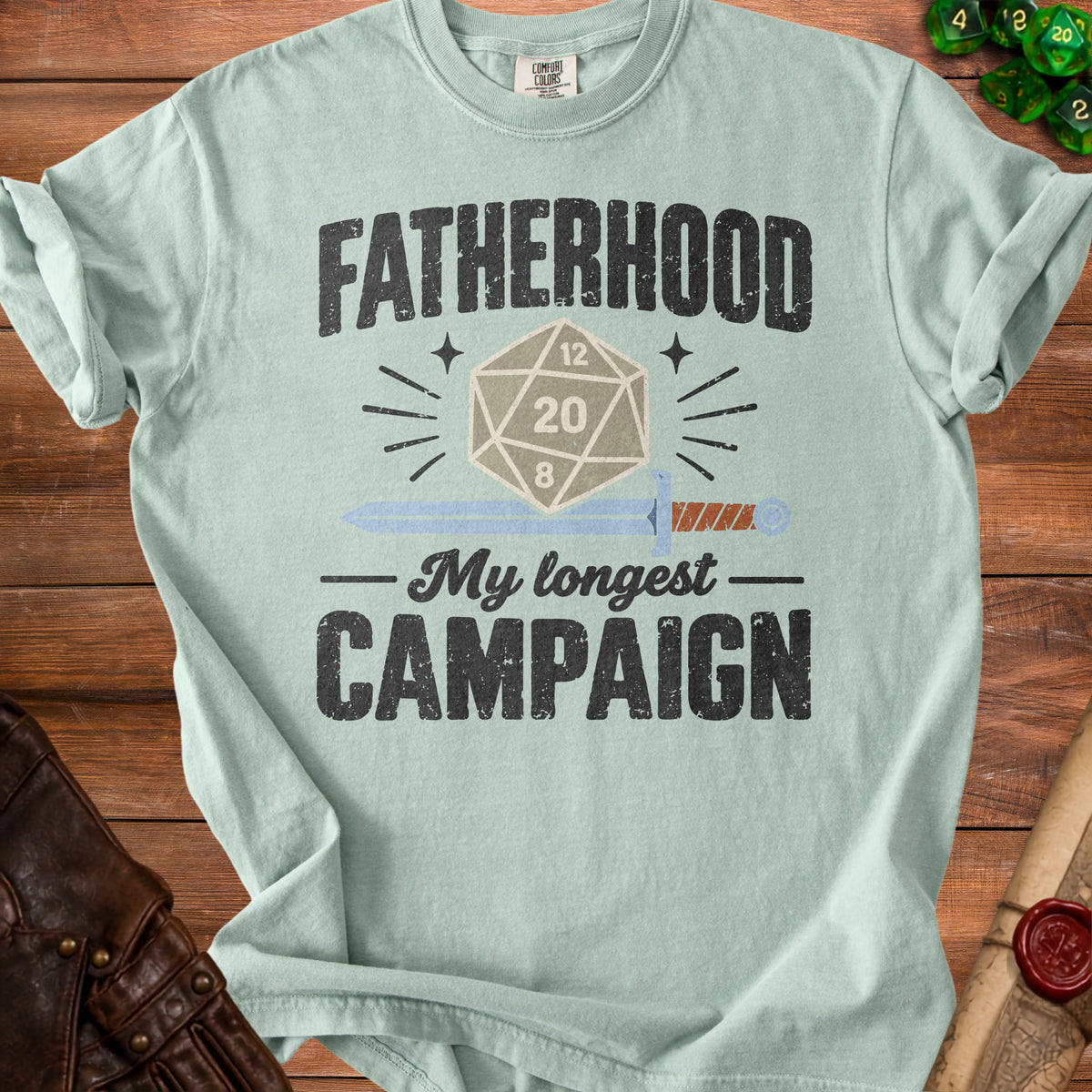 Sage green t-shirt featuring distressed text reading Fatherhood My Longest Campaign with an RPG die and sword.