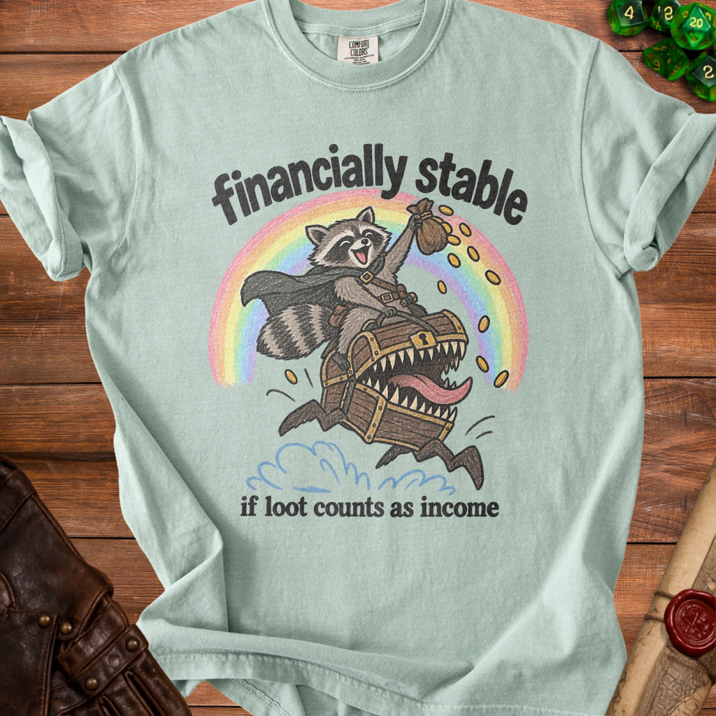 Light teal t-shirt with raccoon on treasure chest, rainbow, and text "financially stable if loot counts as income".