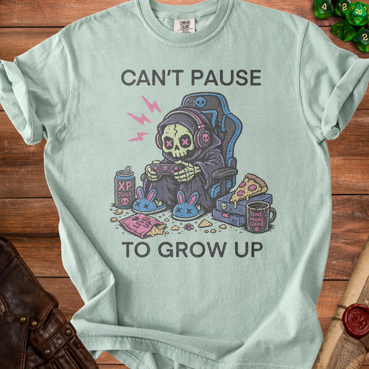 Light blue t-shirt with graphic of a skeleton in a gaming chair, text "Can't Pause To Grow Up".