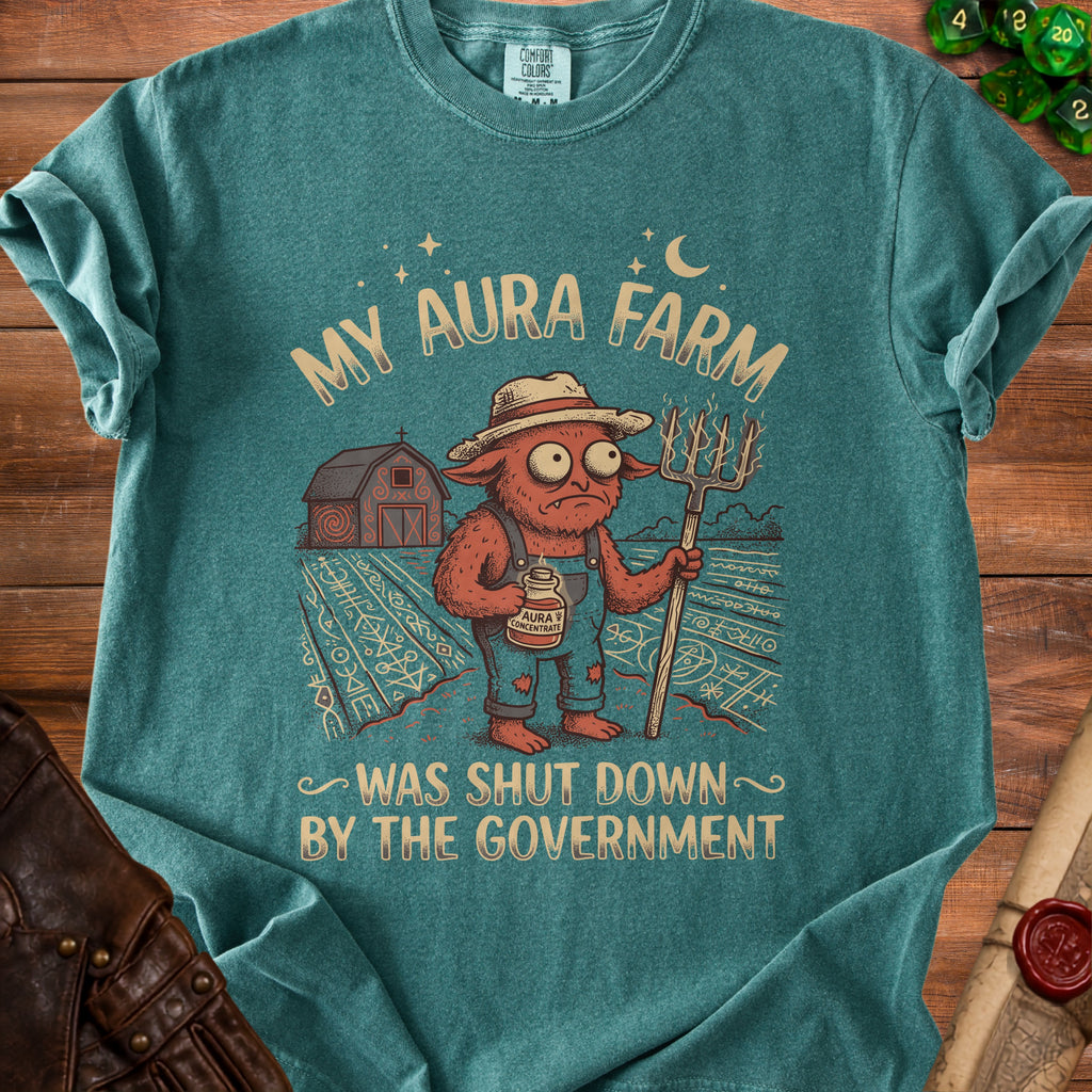 Green t-shirt with a graphic of a red creature holding a pitchfork and "My Aura Farm Was Shut Down By The Government" text.