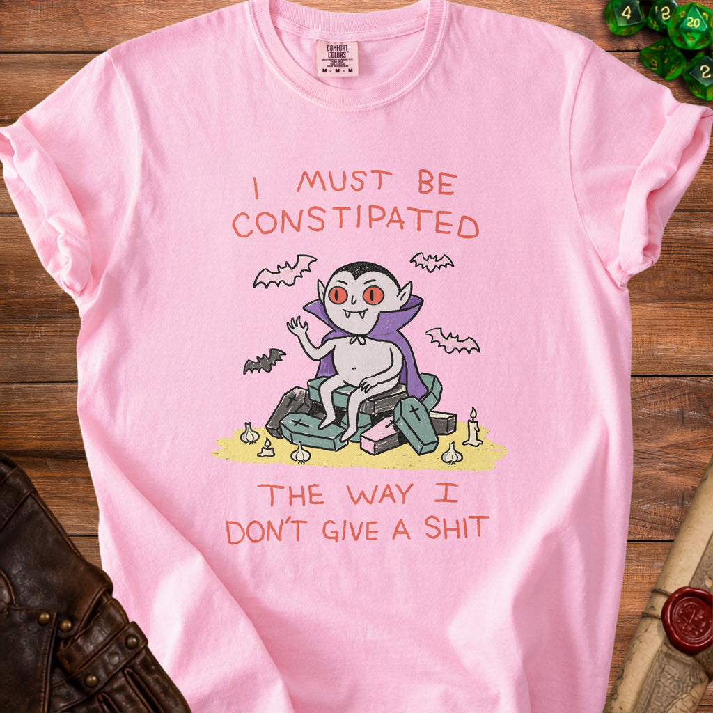 Pink t-shirt with a cartoon vampire sitting on coffins and text about constipation.