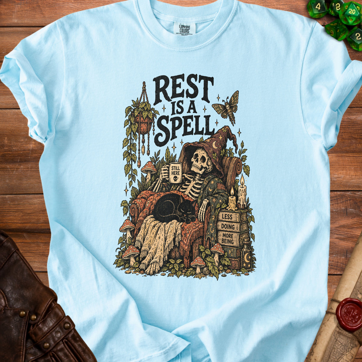 Skeleton relaxing with black cat, text "REST IS A SPELL," "STILL HERE," "LESS DOING MORE BEING."