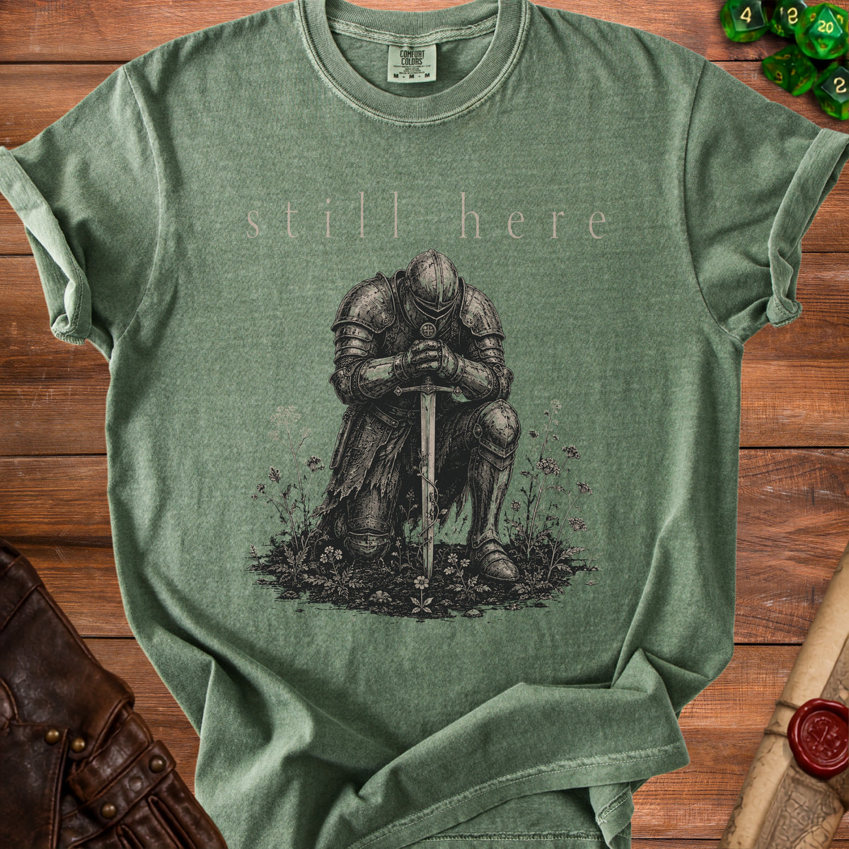 Green t-shirt with kneeling knight and "still here" text.