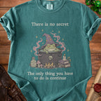 Green t-shirt with wizard frog in cauldron graphic and text: "There is no secret, The only thing you have to do is continue."
