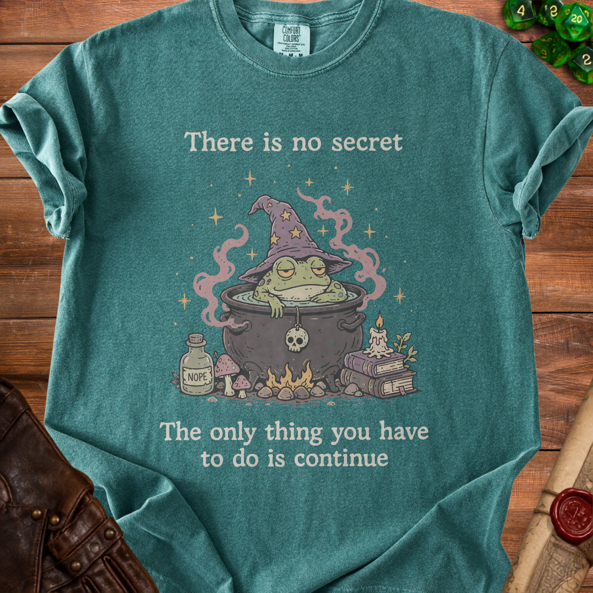 Green t-shirt with wizard frog in cauldron graphic and text: "There is no secret, The only thing you have to do is continue."