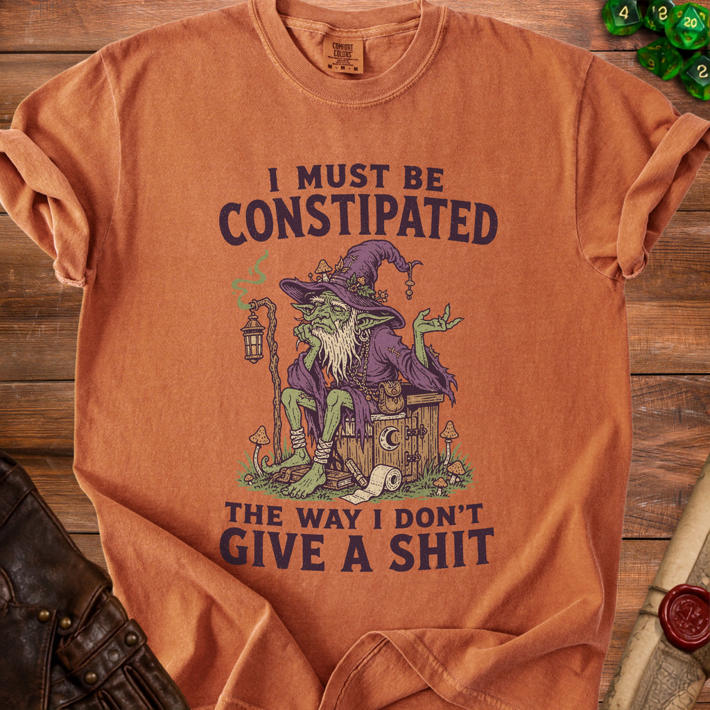 Orange t-shirt with illustration of a goblin on a toilet and text "I MUST BE CONSTIPATED THE WAY I DON'T GIVE A SHIT".