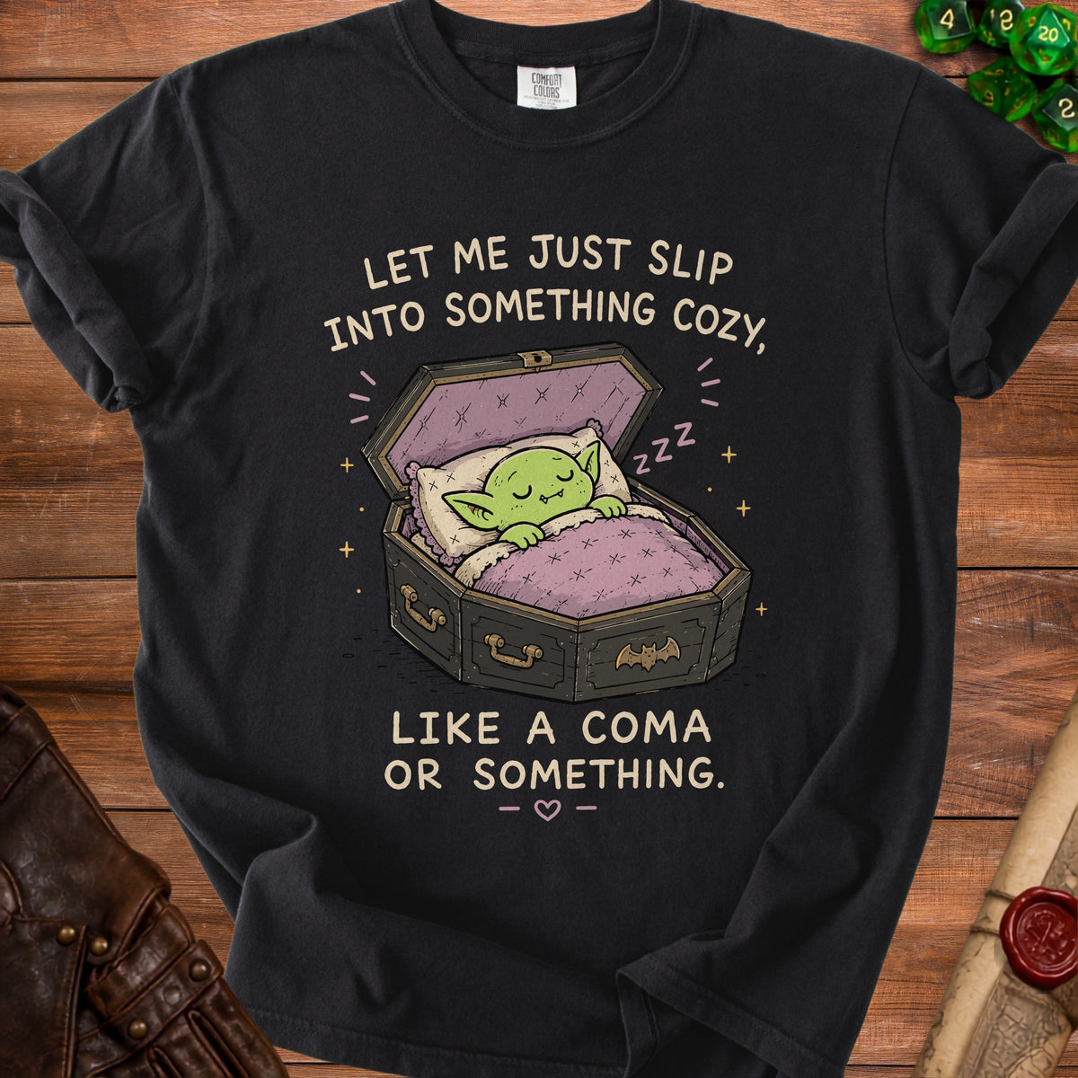Black t-shirt with goblin sleeping in coffin, text "LET ME JUST SLIP INTO SOMETHING COZY, LIKE A COMA OR SOMETHING."
