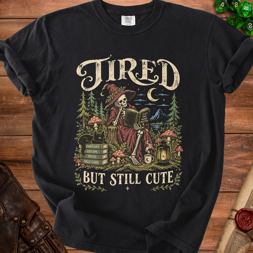 Black t-shirt with skeleton reading a book, "Tired But Still Cute" text.